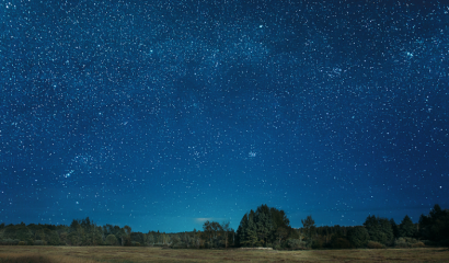 Bright stars light up the night sky over a large field below.