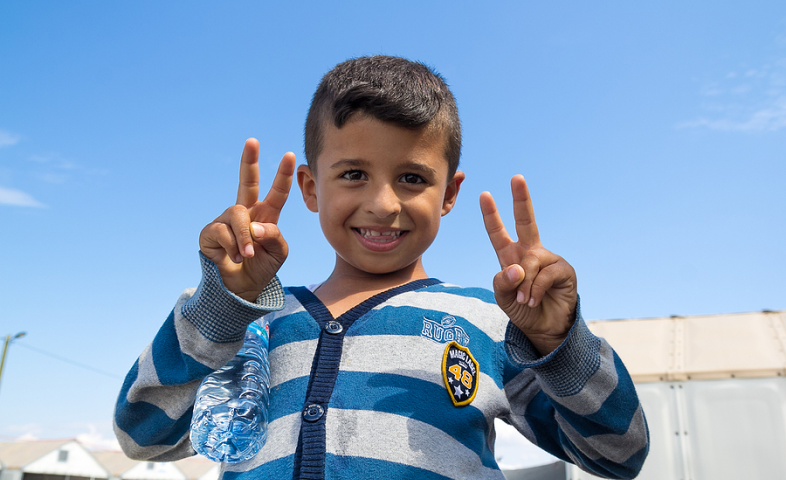 A little boy holds up four fingers and smiles at the camera.