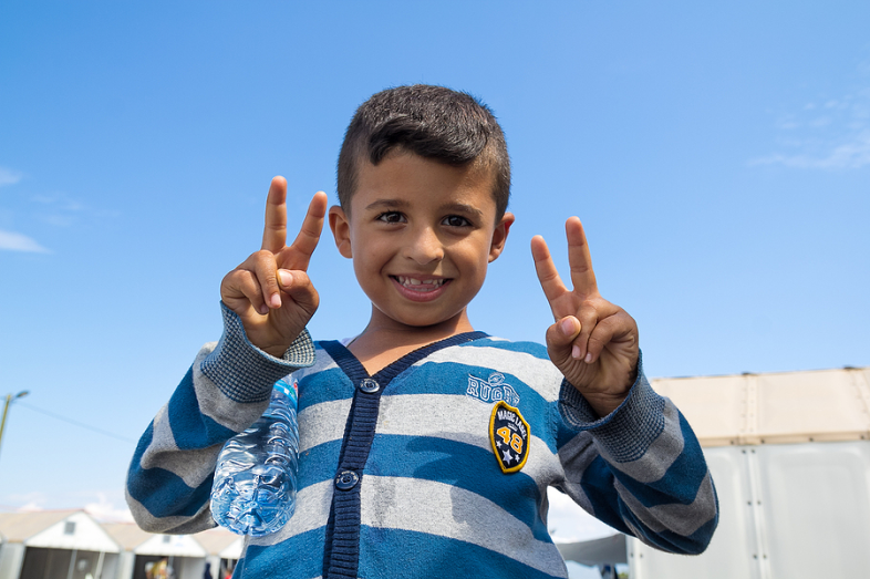 A little boy holds up four fingers and smiles at the camera.