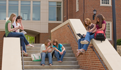 A group of college girls sit on the steps of a campus building.