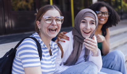 Three multiracial students sit laughing on outdoor steps.