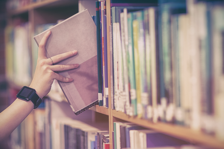 A hand is shown reaching for a book on a bookshelf.