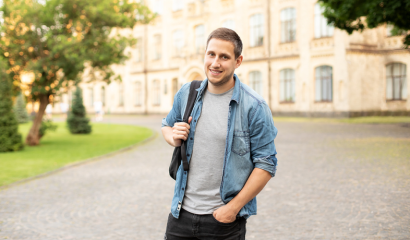 A young male stands on a college campus, with a building in the background.