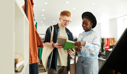 Two young adults stand in a retail store, staring at books they're holding.