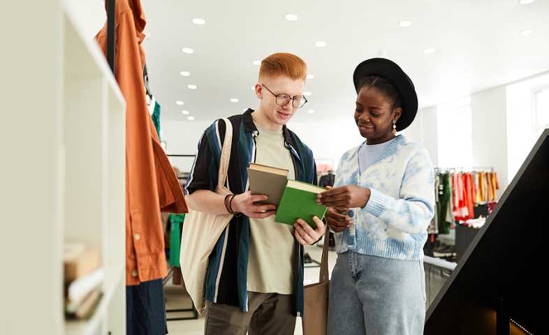 Two young adults stand in a retail store, staring at books they're holding.