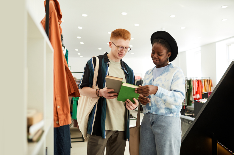 Two young adults stand in a retail store, staring at books they're holding.