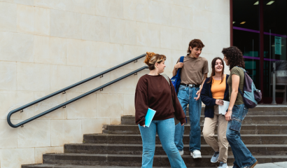 A group of college students walk down stairs and speak with each other outside their school.