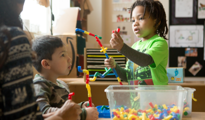 Two small children play with toys that connect to each other.