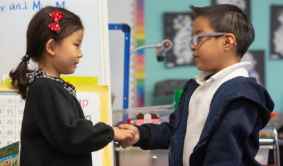 A kindergarten age girl and boy shake hands.