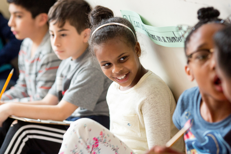 Elementary-aged school children sit and speak to each other.