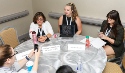 A group of women sit around a table having a conversation.