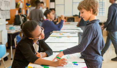 Two elementary age kids chat over artwork in school.