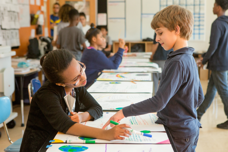 Two elementary age kids chat over artwork in school.