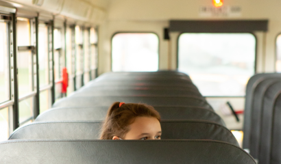 A elementary-aged girl sits alone on an empty school bus.