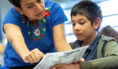 A teacher points out something on a piece of paper a student places in her view.