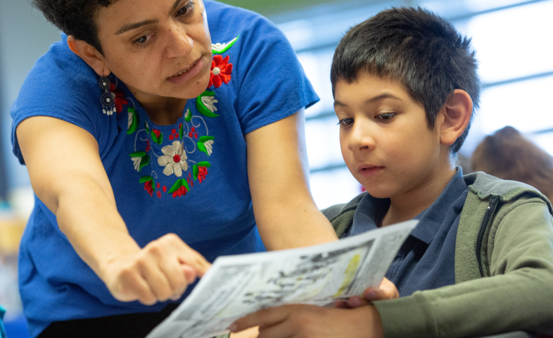 A teacher points out something on a piece of paper a student places in her view.