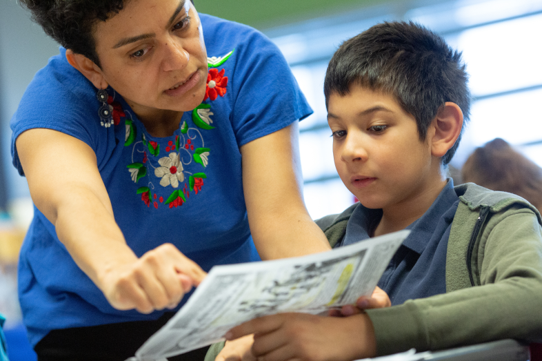 A teacher points out something on a piece of paper a student places in her view.