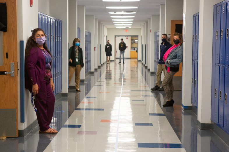 Teachers and students wearing face masks stand in a school hallway.